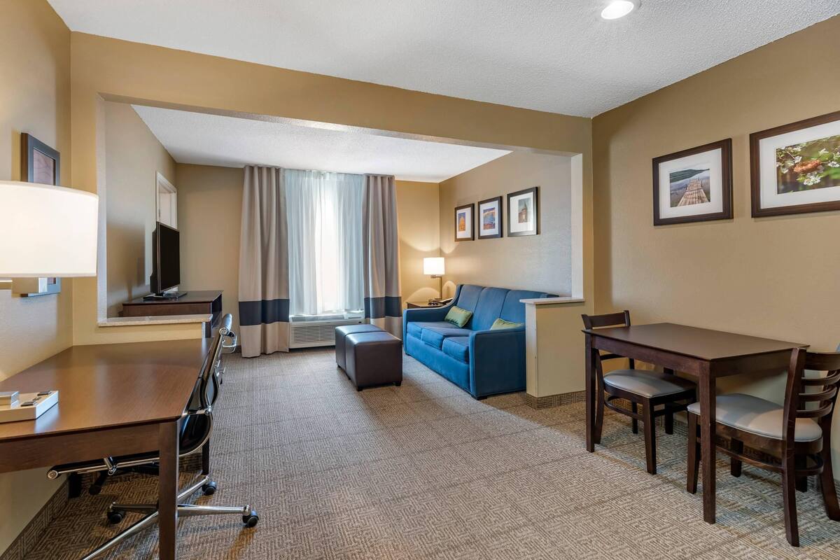 A hotel room with a desk, a sofa, a dining table, and a TV.
