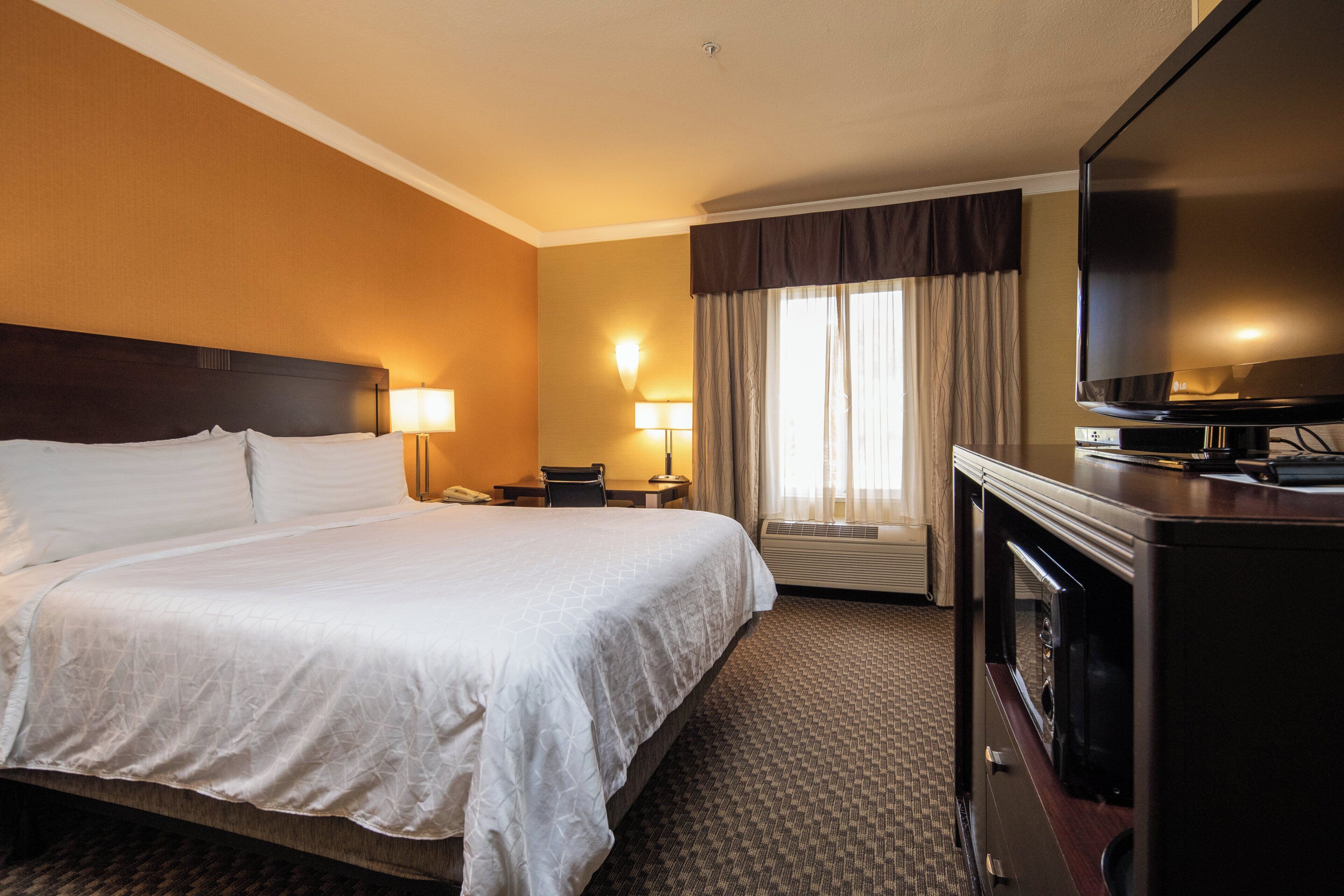 Une chambre d’hôtel avec un grand lit, un téléviseur à écran plat, un bureau avec une chaise et une fenêtre avec des rideaux.