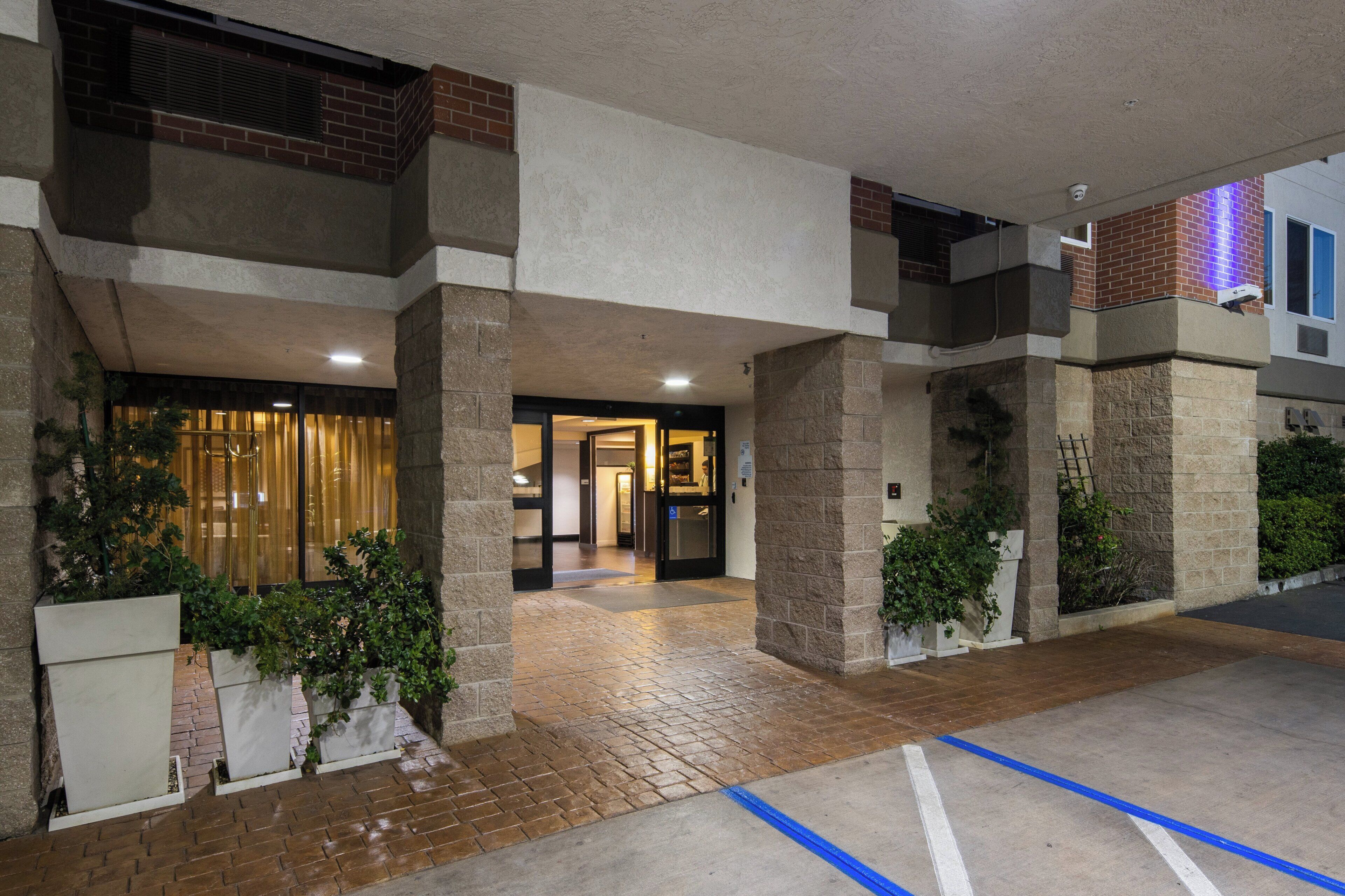 A building entrance with a brick facade, a glass door, and potted plants.
