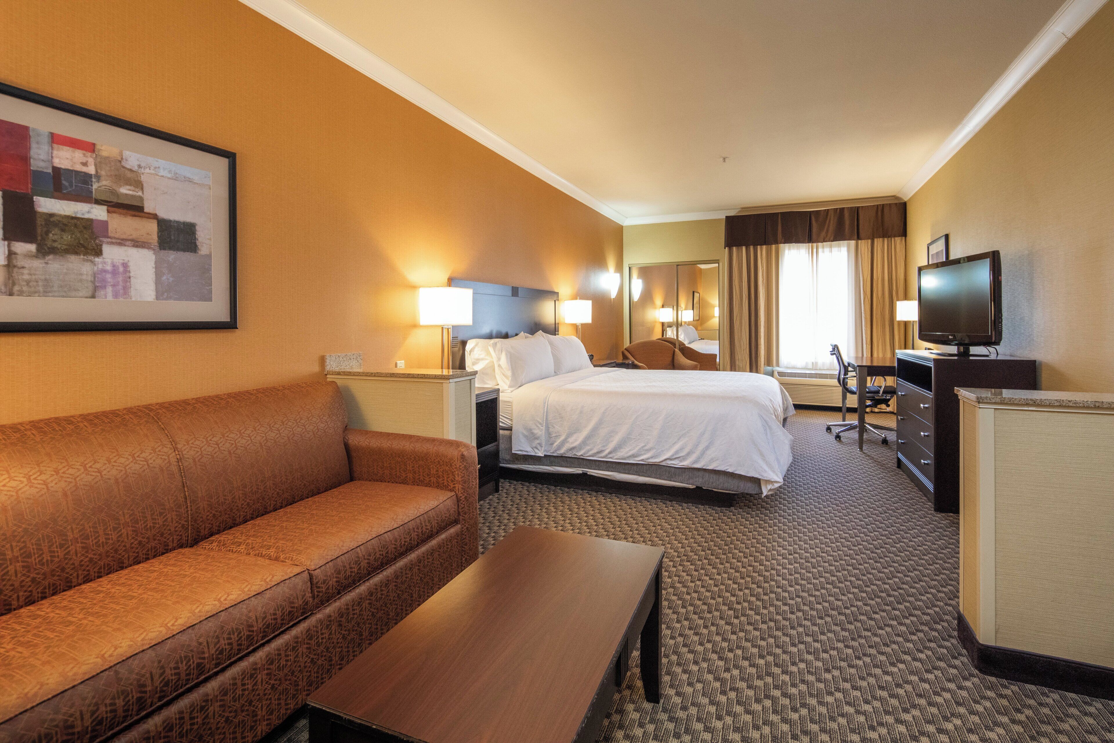 A hotel room with a king-sized bed, a sofa, a desk, a television, and a painting on the wall.