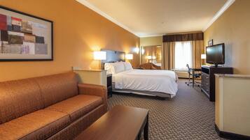 A hotel room with a king-sized bed, a sofa, a desk, a television, and a painting on the wall.