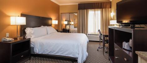 A hotel room with a large bed, bedside lamps, a desk with a computer, a television, and a mirror.