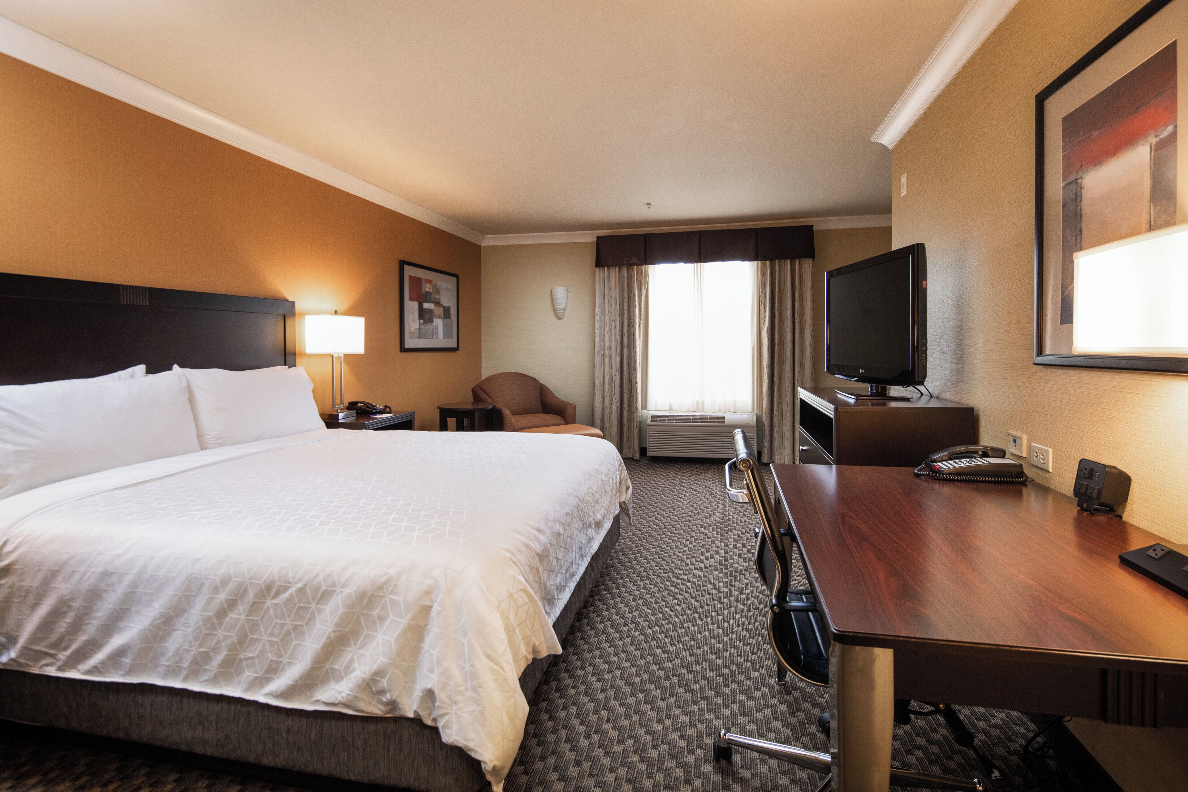 A hotel room with a large bed, a desk with a chair, a television, and a window with curtains.