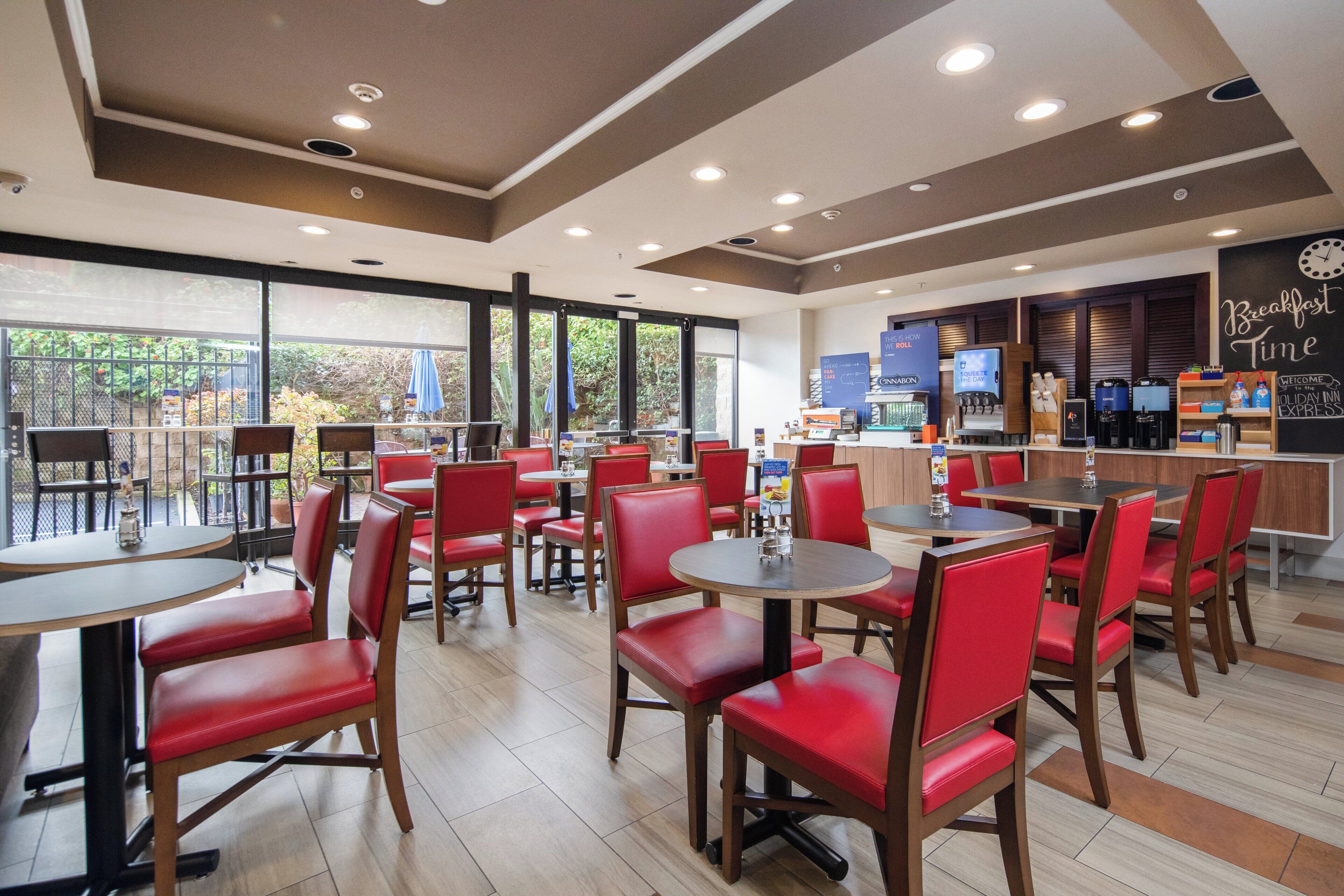 A restaurant with red chairs and tables, a counter with a coffee machine, and a view of greenery outside.