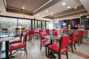 A restaurant with red chairs and tables, a counter with a coffee machine, and a view of greenery outside. - Holiday Inn Express Castro Valley - I-580 by IHG (Castro Valley)