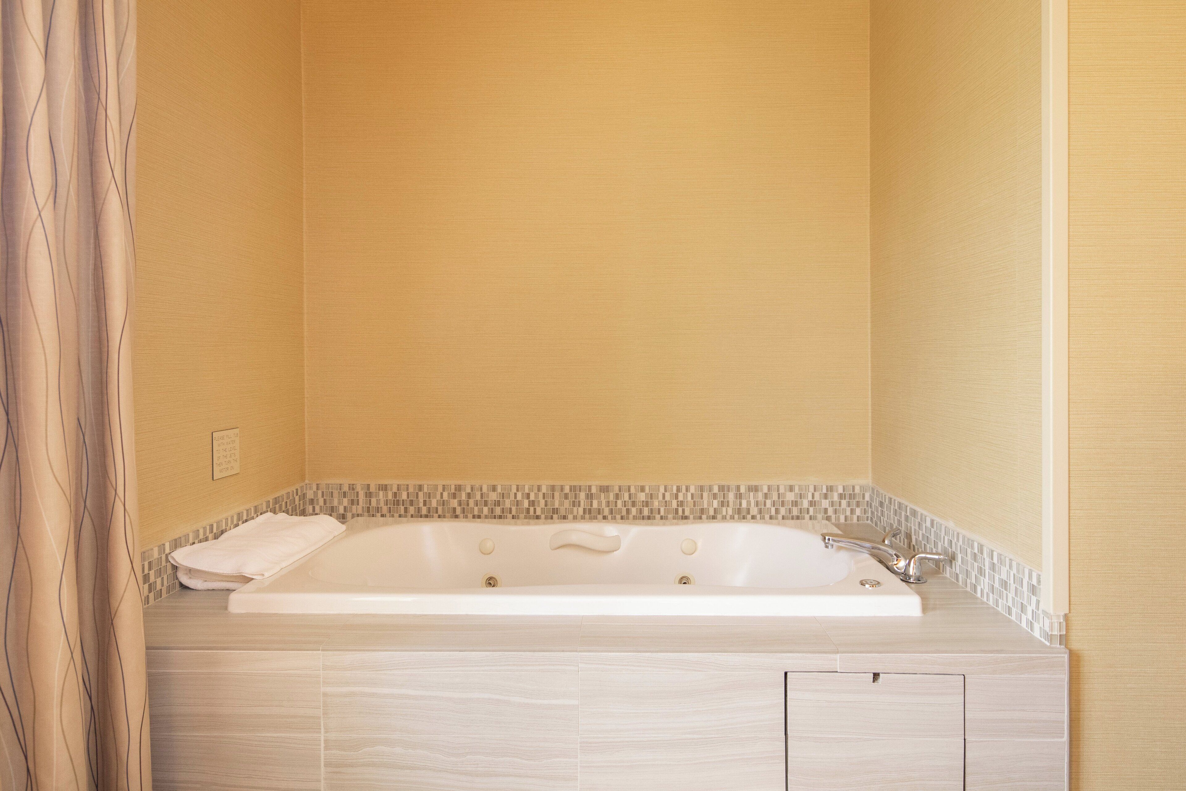 Un baño con bañera, una toalla y piso de baldosas.