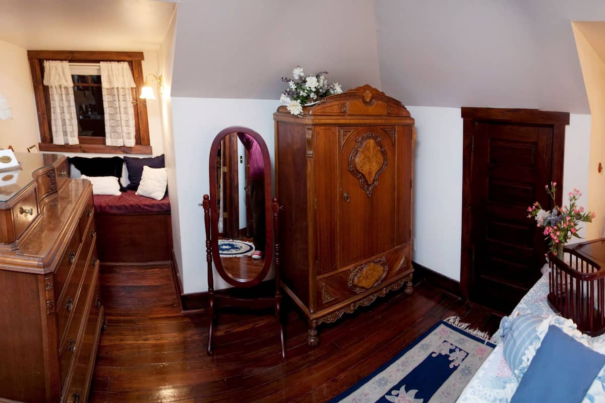 Une chambre à coucher avec une commode en bois, une coiffeuse avec un miroir, un lit recouvert d’une courtepointe et une table de chevet avec une lampe.