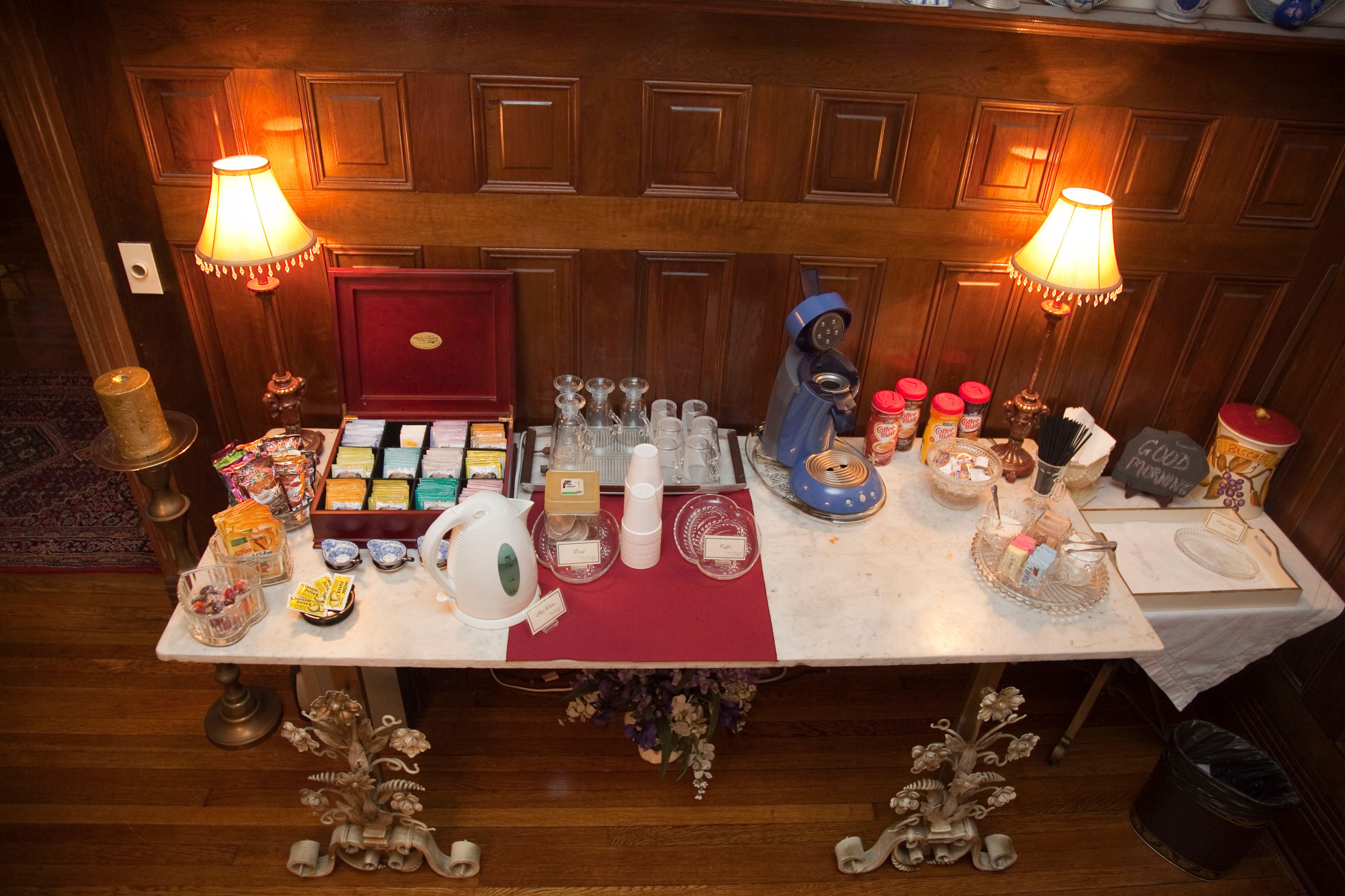A table set with various food items, glassware, and a coffee machine, indicating a self-service breakfast area.