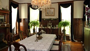 A dining room with a chandelier, wooden chairs, a table with a lace tablecloth, and potted plants. - Beall Mansion An Elegant Bed & Breakfast Inn (Alton)