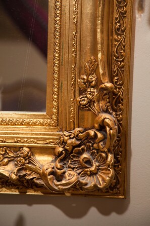 A close-up of an ornate, gold-framed mirror with intricate floral and scroll designs.