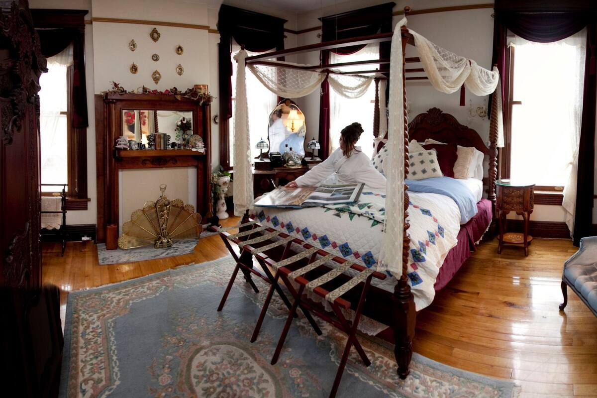 Une chambre à coucher de style traditionnel, avec un lit à baldaquin, un coin salon comprenant une chaise et une table, ainsi qu’une table de chevet avec une lampe.