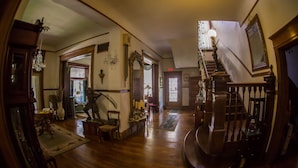 A spacious room with a wooden staircase, a chandelier, and a large mirror. - Beall Mansion An Elegant Bed & Breakfast Inn (Alton)