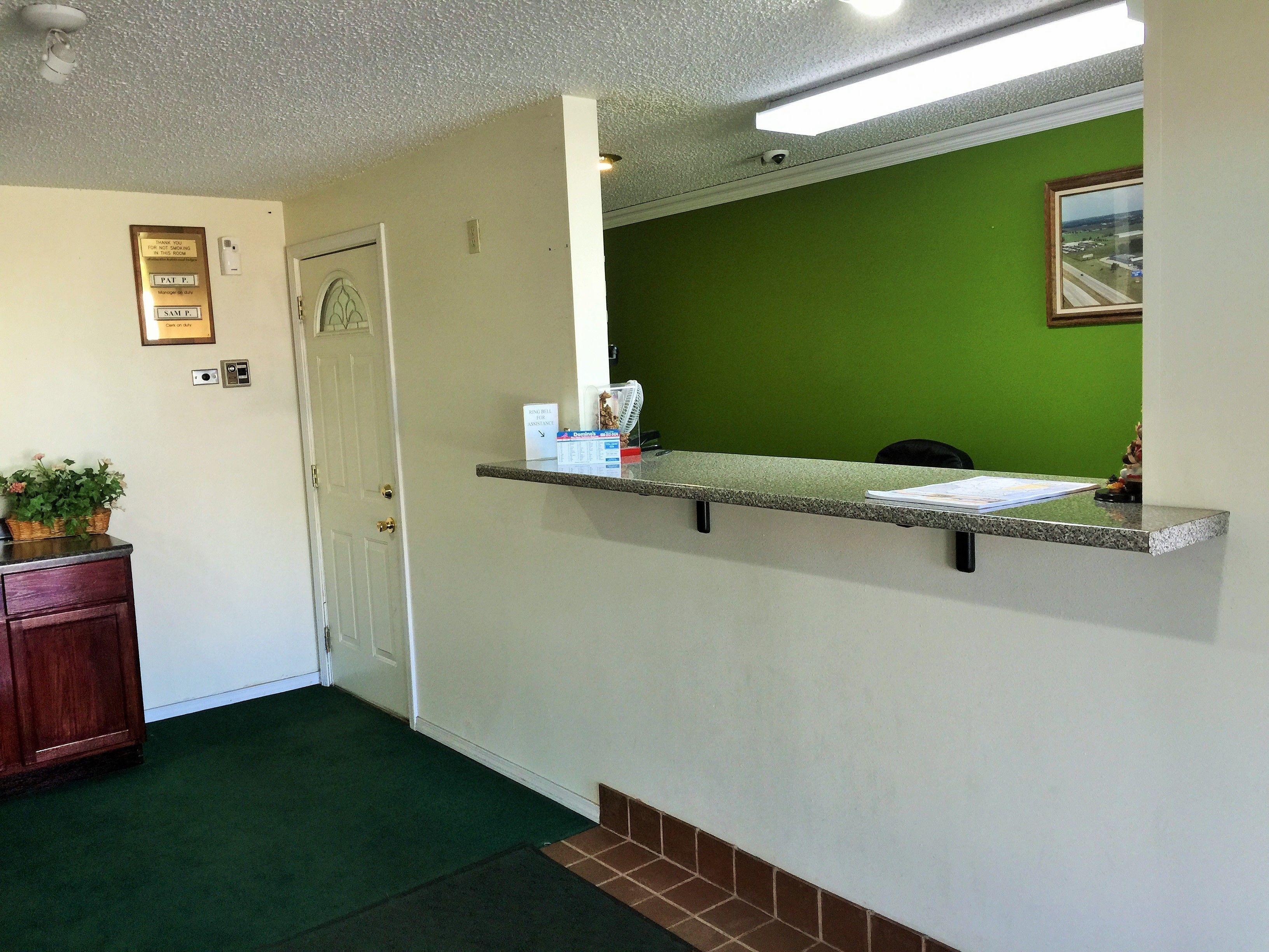 A reception area with a green wall, a reception desk, a door, and a small plant on a cabinet.