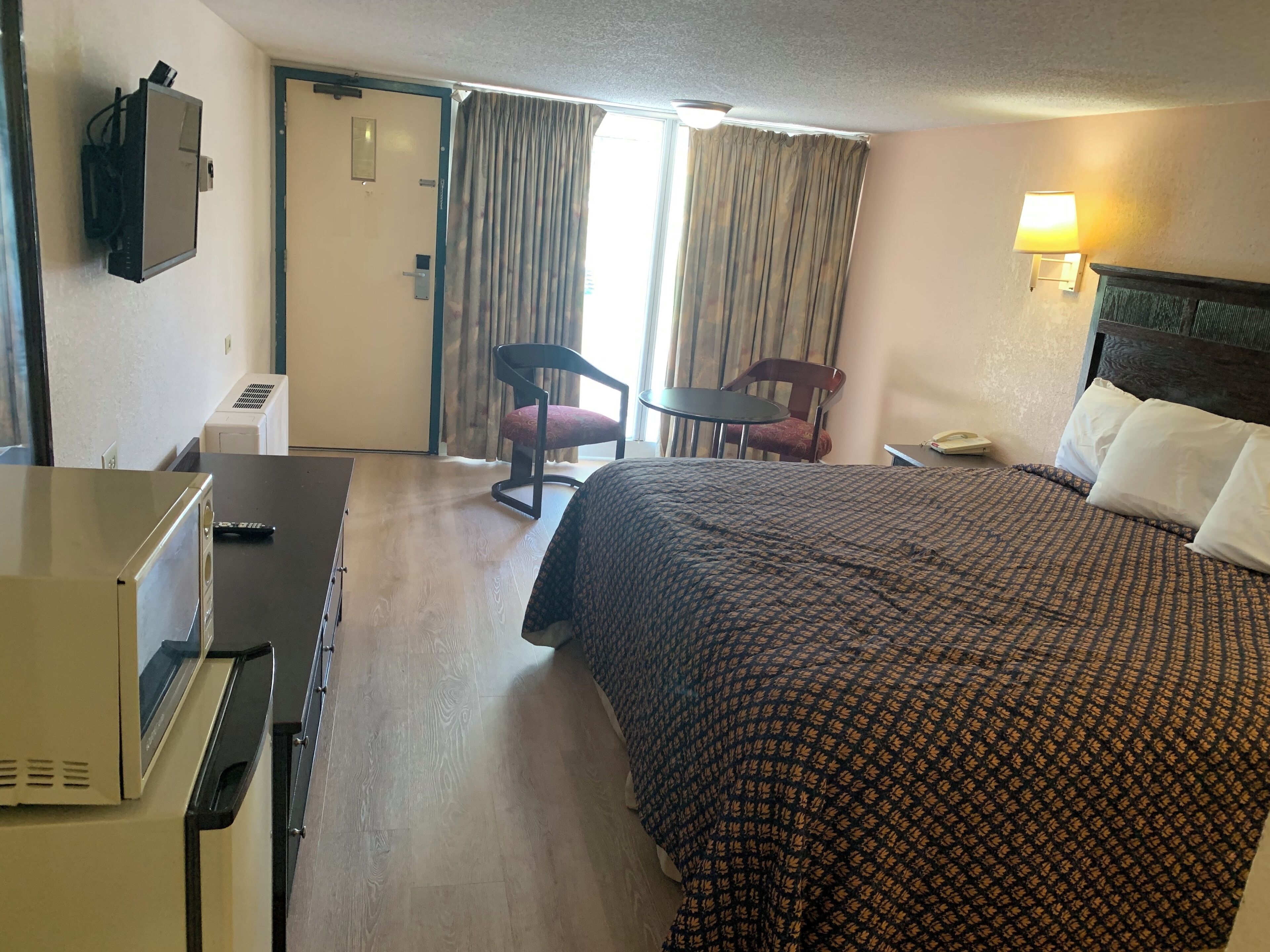 Ett hotellrum med en säng, ett skrivbord, en stol, en lampa och en telefon.