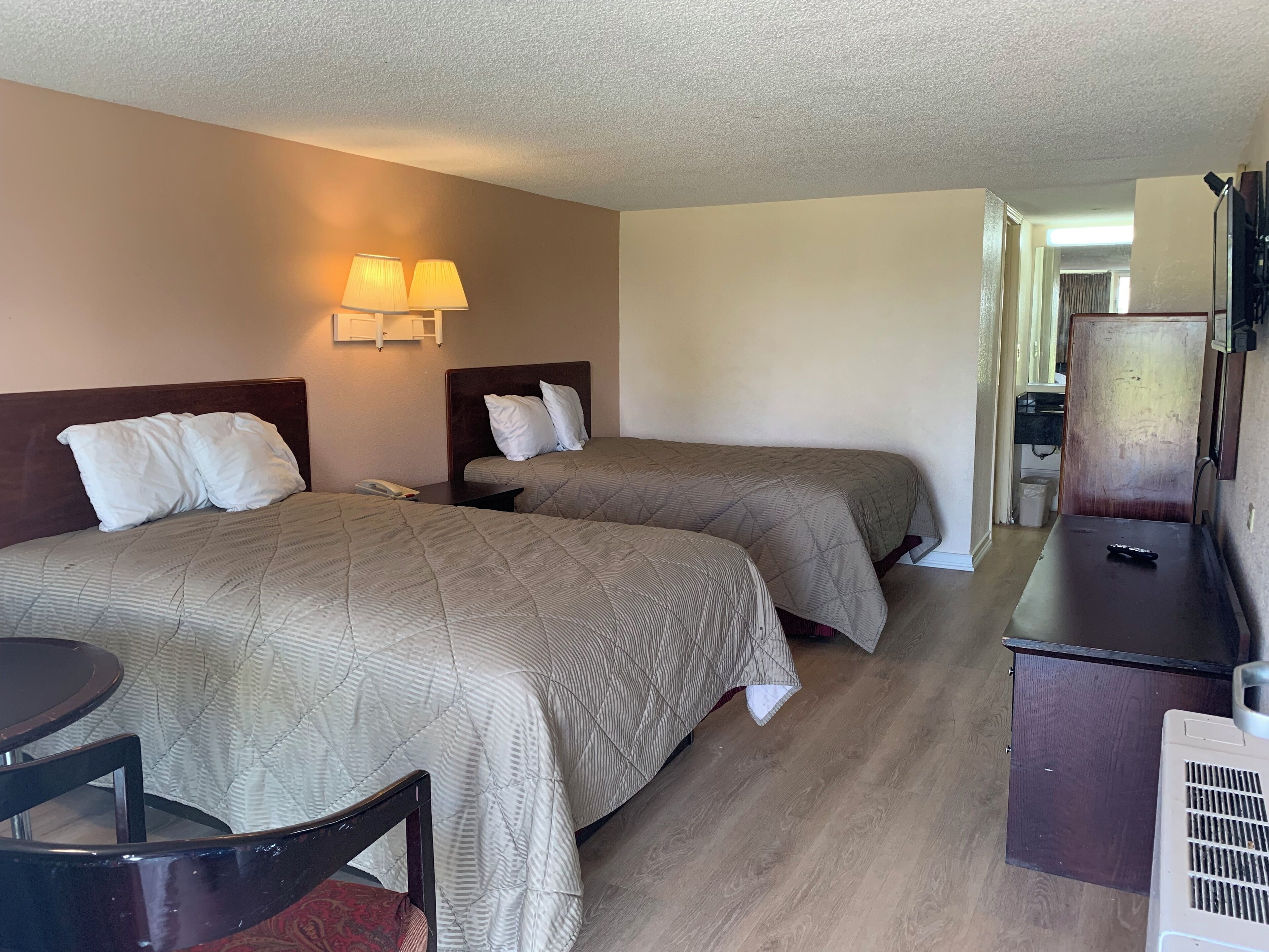 A hotel room with two beds, a desk, a chair, a phone, and a lamp.