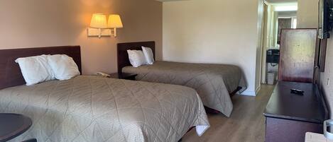 A hotel room with two beds, a desk, a chair, a phone, and a lamp.