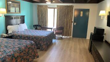Una habitación de hotel con dos camas, un escritorio, una silla, un televisor y una puerta.