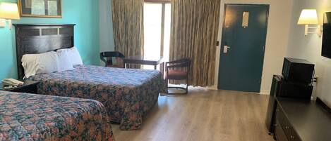 A hotel room with two beds, a desk, a chair, a TV, and a door.