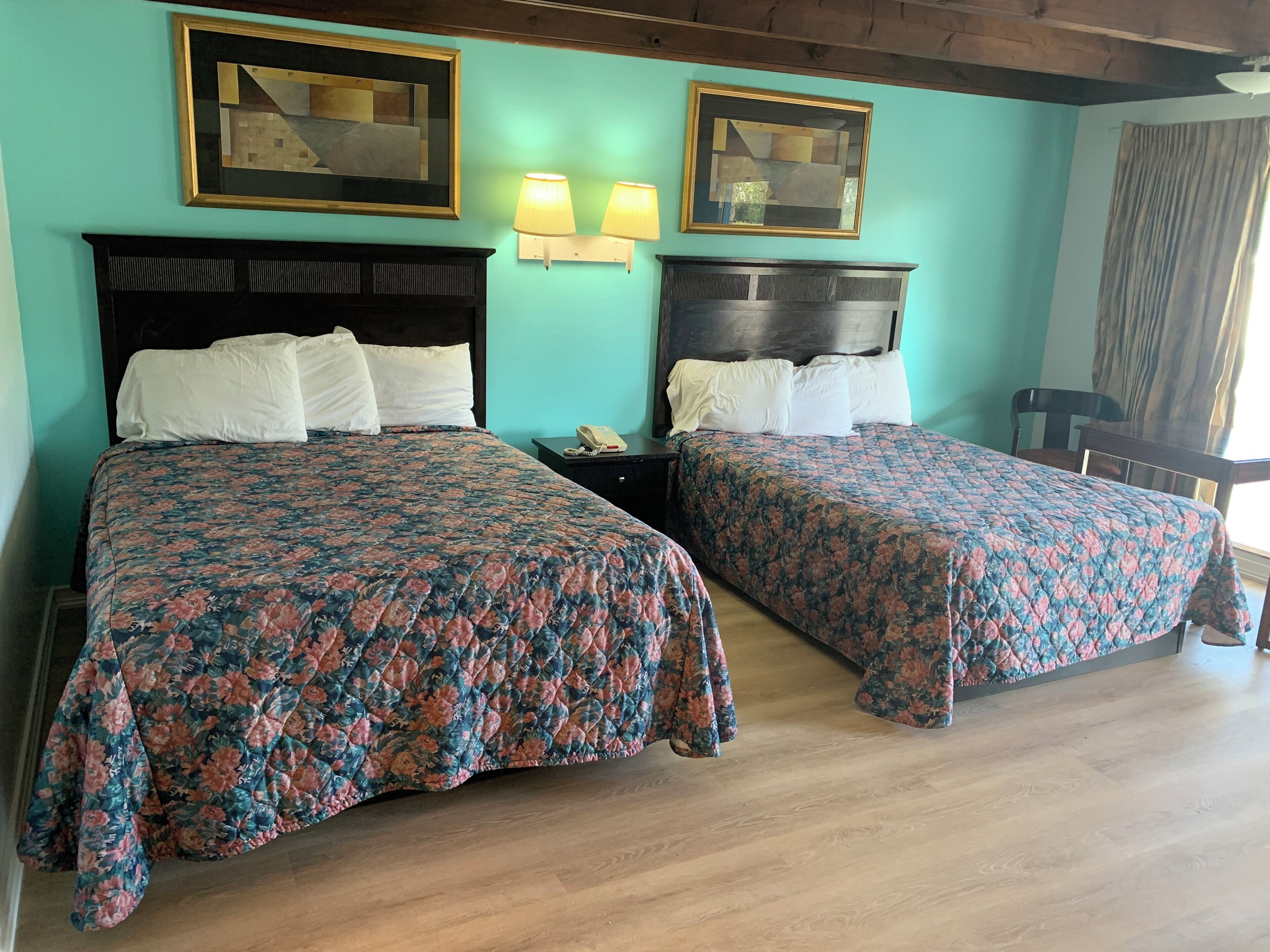 A hotel room with two beds, each with a floral bedspread, a wooden headboard, and a nightstand with a lamp.