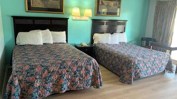 A hotel room with two beds, each with a floral bedspread, a wooden headboard, and a nightstand with a lamp.