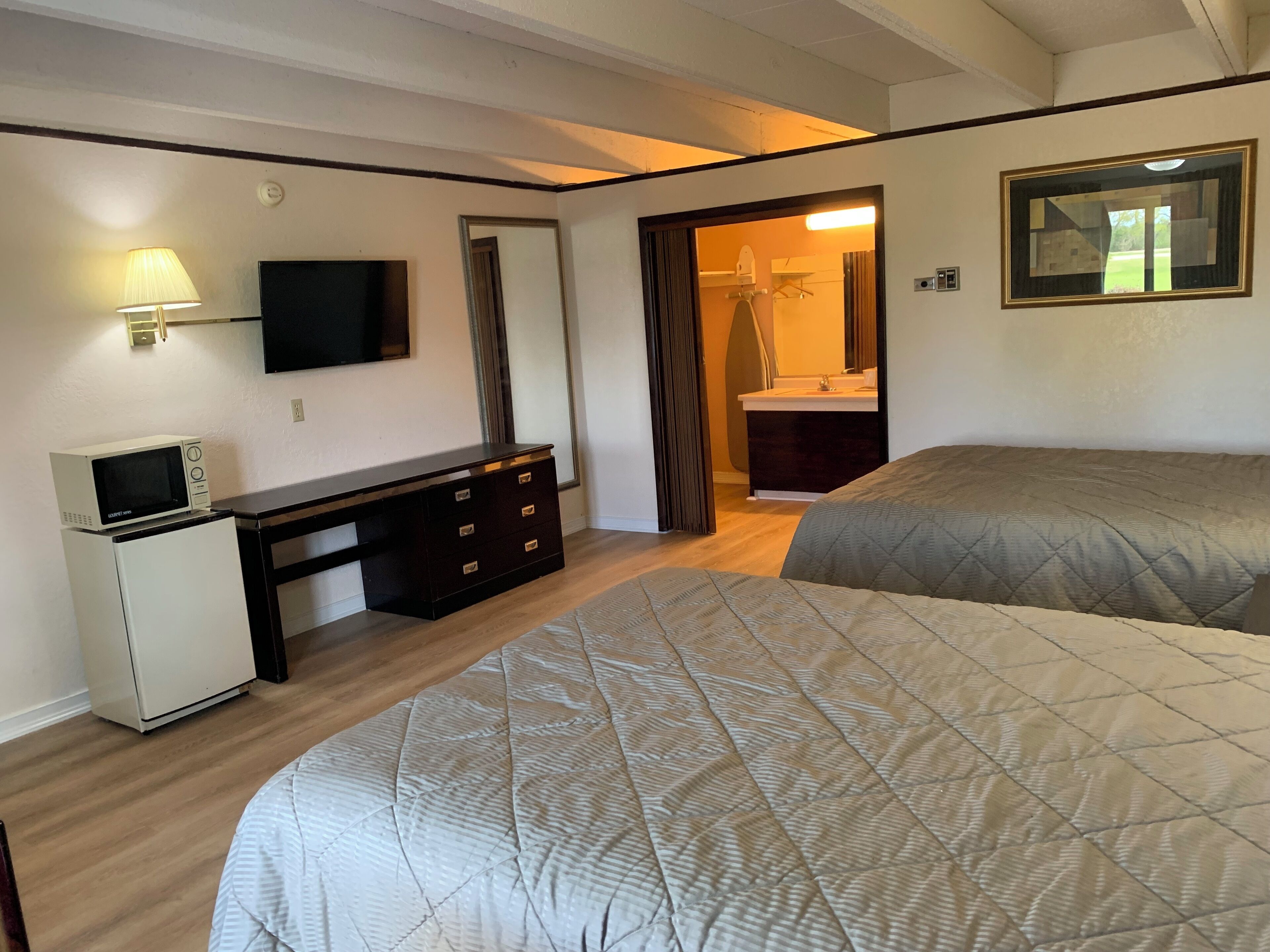 A hotel room with two beds, a desk with a microwave, a TV, and a bathroom visible through an open door.