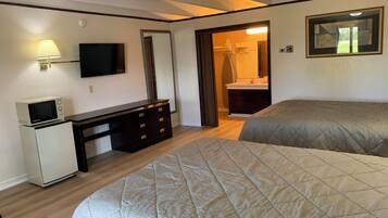 A hotel room with two beds, a desk with a microwave, a TV, and a bathroom visible through an open door.