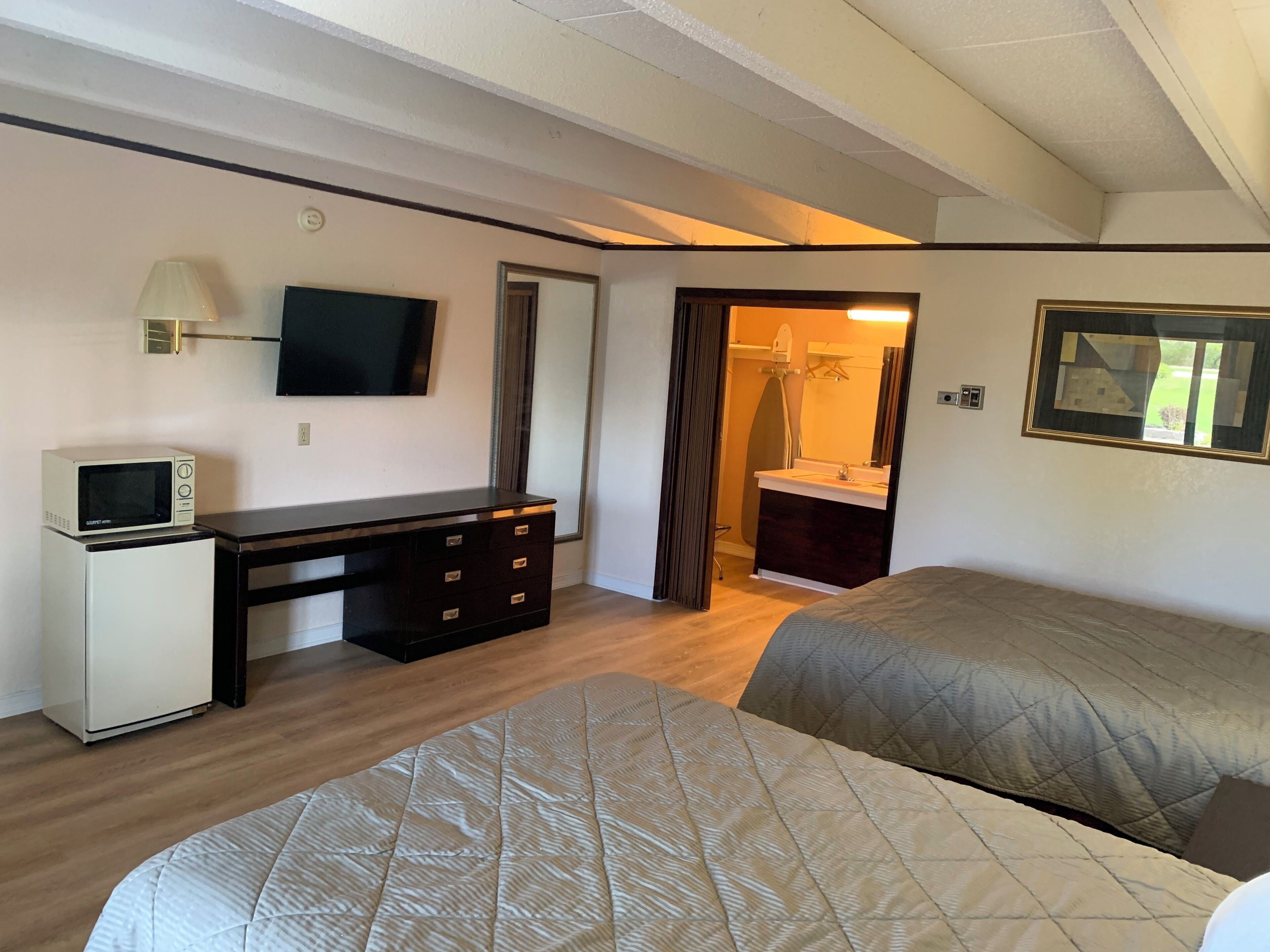 A compact hotel room with a bed, a desk with a television, a small kitchenette, and a bathroom visible through an open door.