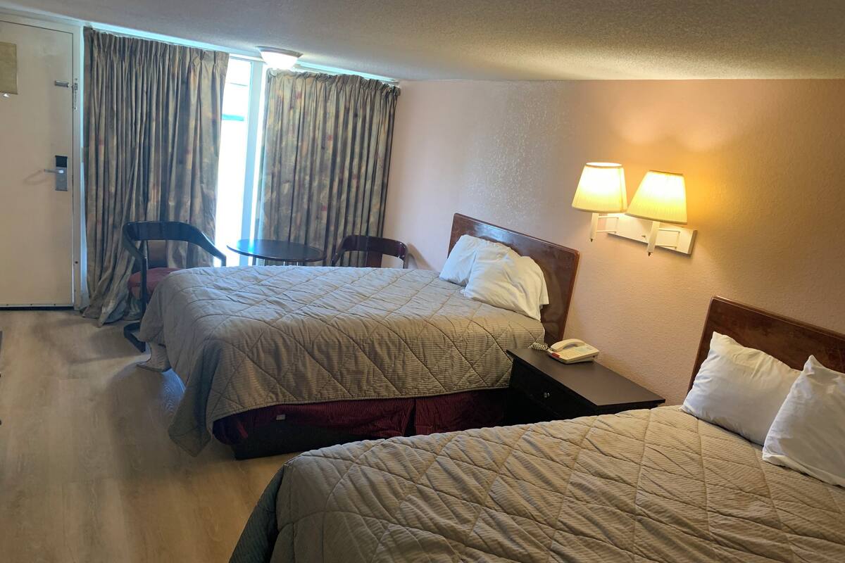 A hotel room with two beds, a desk, a chair, a lamp, and a phone on the desk.