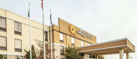 Un hotel La Quinta con un llamativo logo de sol, una zona de estacionamiento techada y un asta con la bandera estadounidense.