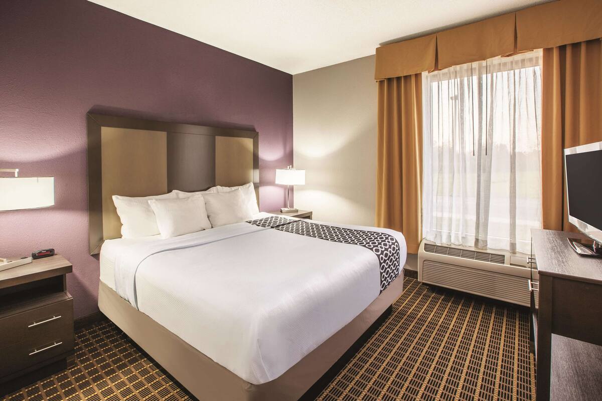Une chambre d’hôtel avec un grand lit, deux tables de chevet, un bureau avec un ordinateur et une fenêtre avec des rideaux.
