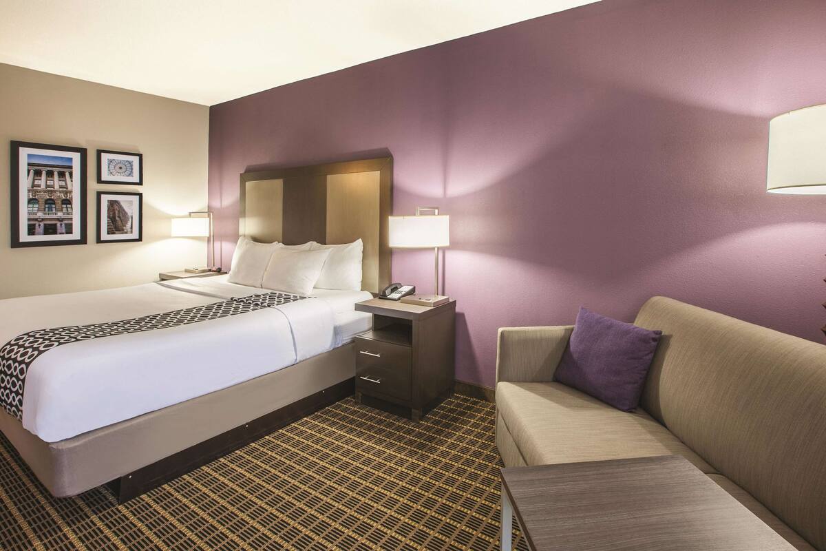Une chambre d’hôtel avec un lit, une table de chevet, un canapé et une moquette à motifs.
