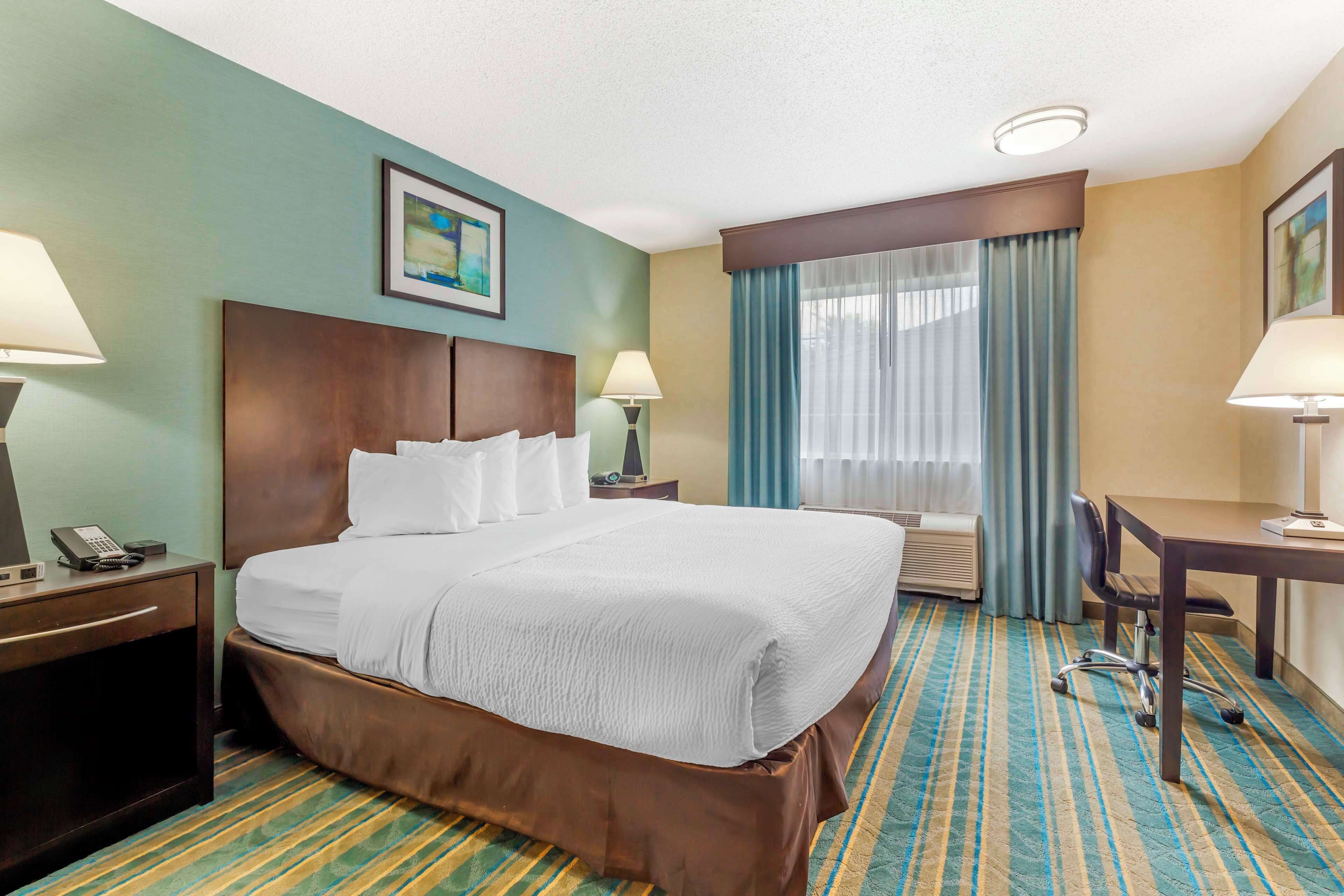 Habitación de hotel con una cama grande, dos mesitas de noche con lámparas, un escritorio con una silla y una ventana con cortinas.