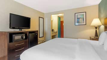 A hotel room with a bed, a television, a microwave, a desk, a lamp, and a door leading to a bathroom.