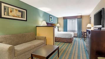 Quarto de hotel com sofá, cama, escrivaninha, televisão e banheiro.
