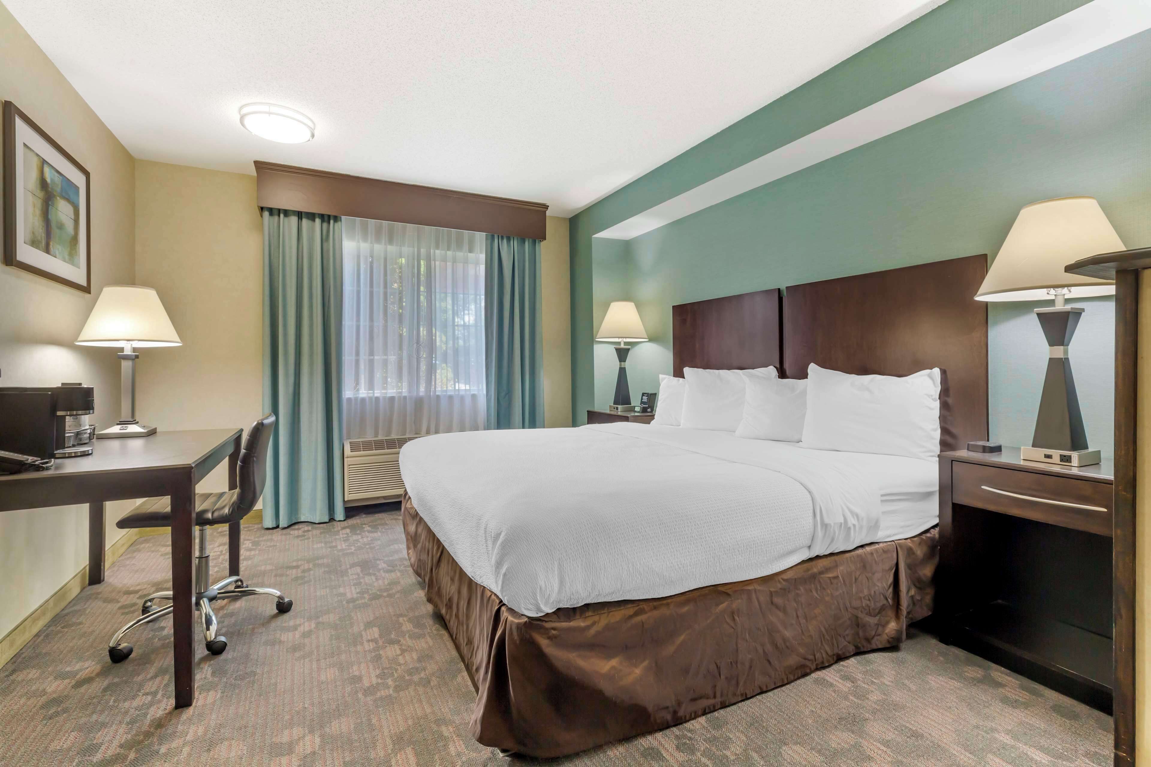 Habitación de hotel con una cama grande, un escritorio con silla, dos lámparas de noche y una ventana con cortinas.