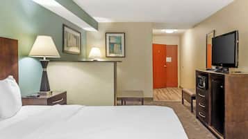 Una habitación de hotel con cama, mesita de noche, lámparas, escritorio, televisor y armario.