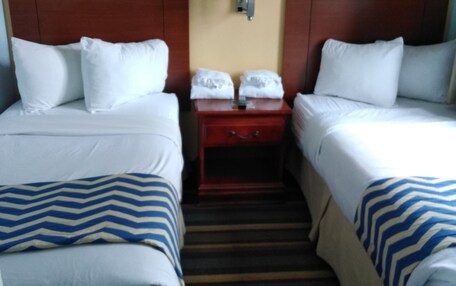 A hotel room with two beds, a nightstand with a lamp, and a clock on the wall.