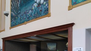 A reception desk with a green counter, wooden paneling, and a framed painting above. - Travelodge by Wyndham Bishop (Bishop)
