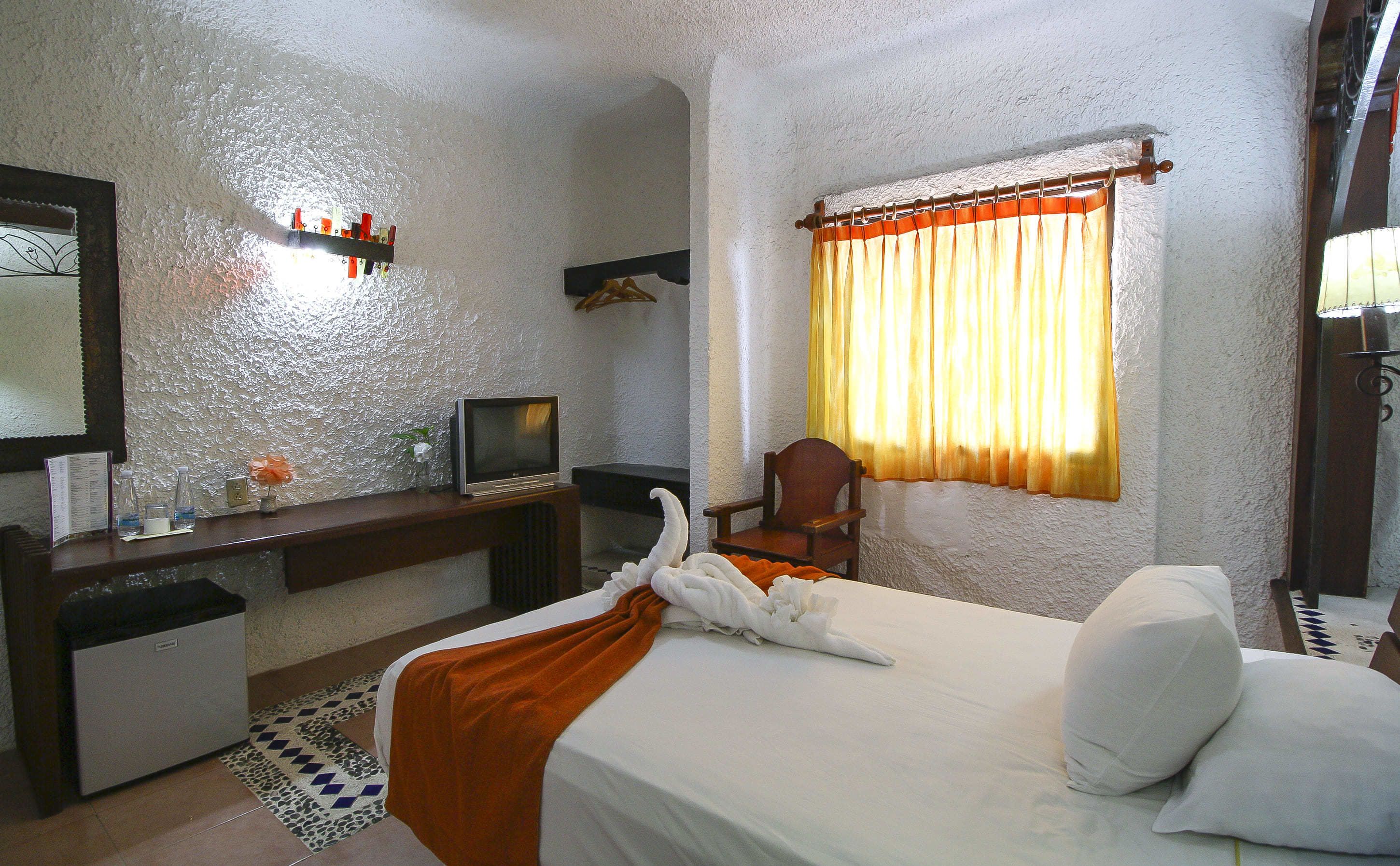 Une chambre d’hôtel avec un lit, un bureau avec une télévision, une chaise et une fenêtre avec des rideaux.