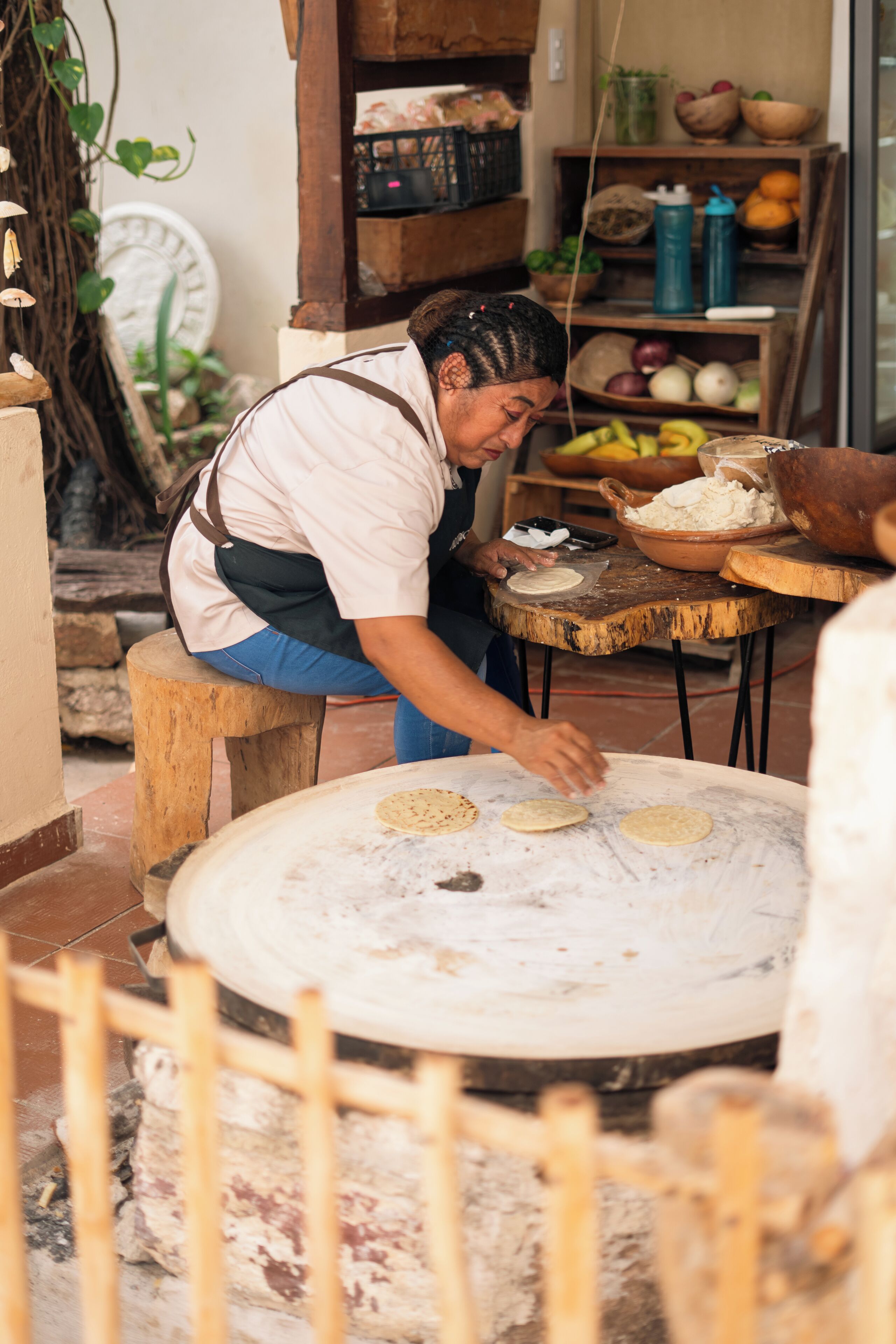 Une personne prépare des tortillas sur une grande plaque de cuisson ronde dans une cuisine rustique.