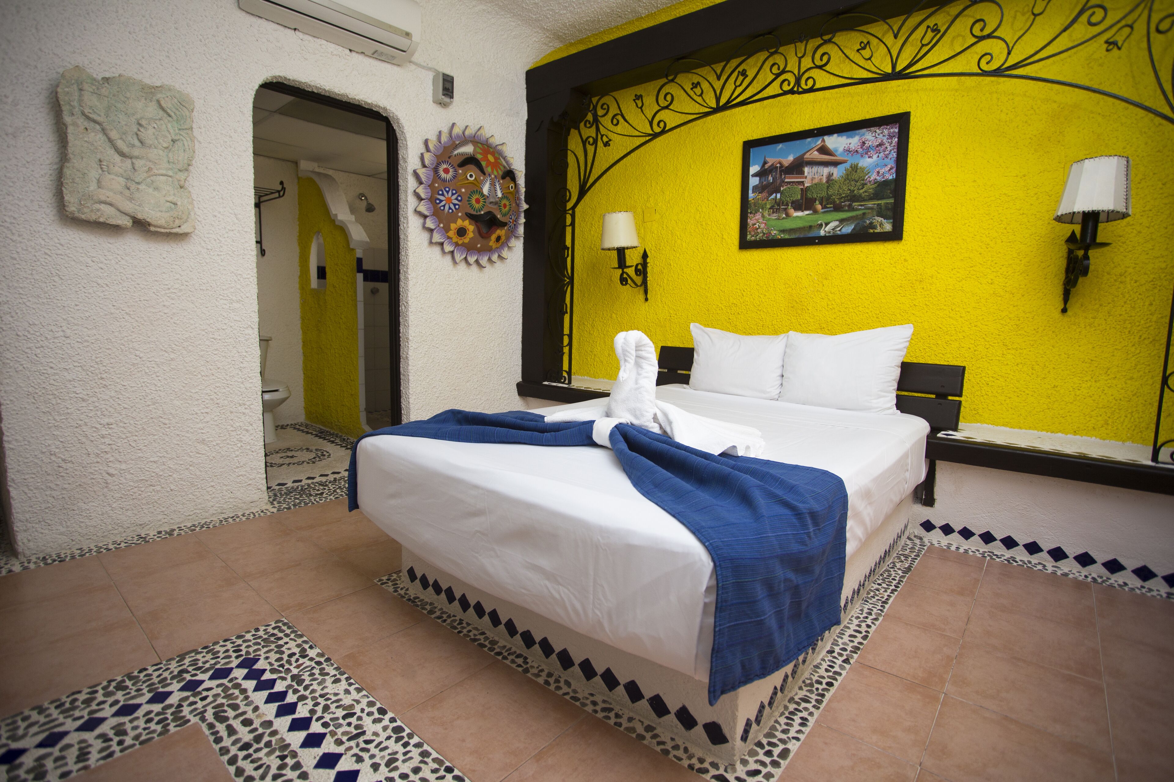 Habitación de hotel con una cama, dos mesitas de noche, una lámpara de pared y un adorno mural.