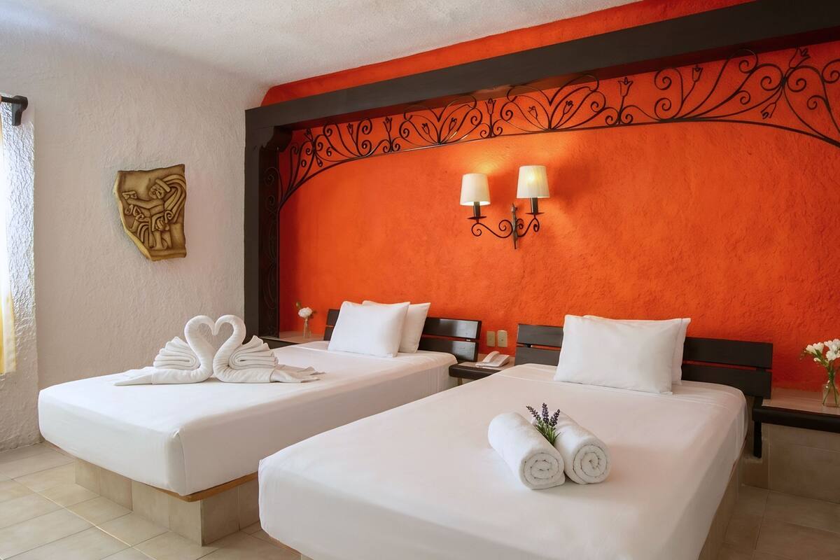 Una camera d'albergo con due letti, un pannello decorativo, un tavolino e un vaso con fiori.