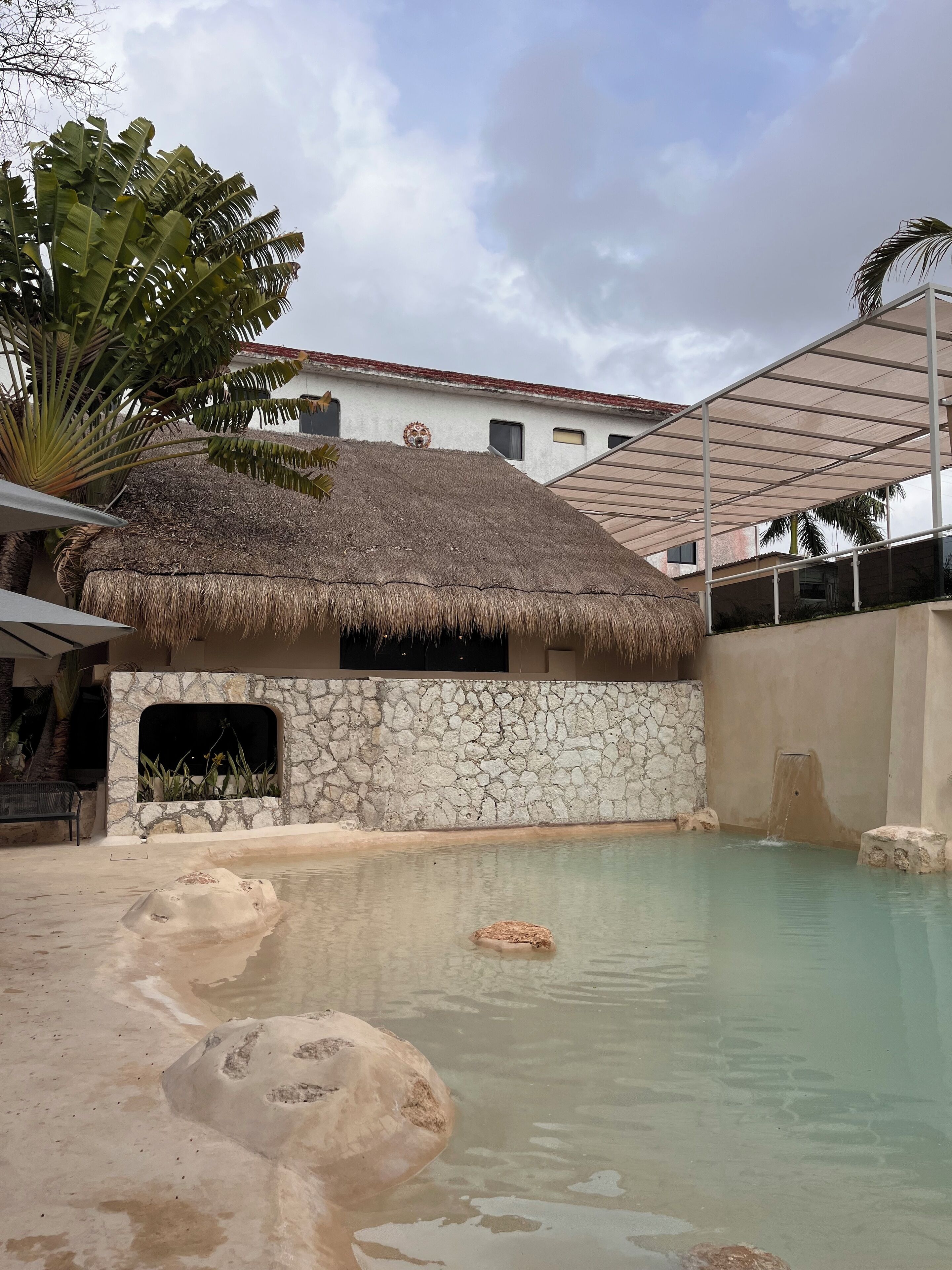 Zona de piscina amb una estructura de palla, parets de pedra i un cel serè.
