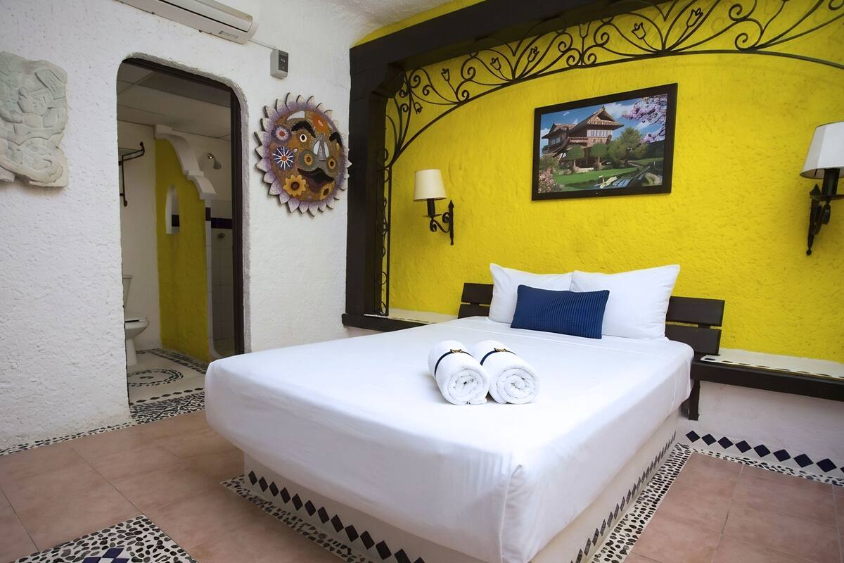 Camera d'albergo con un letto, due abat-jour, una TV a muro e un elemento decorativo a parete.
