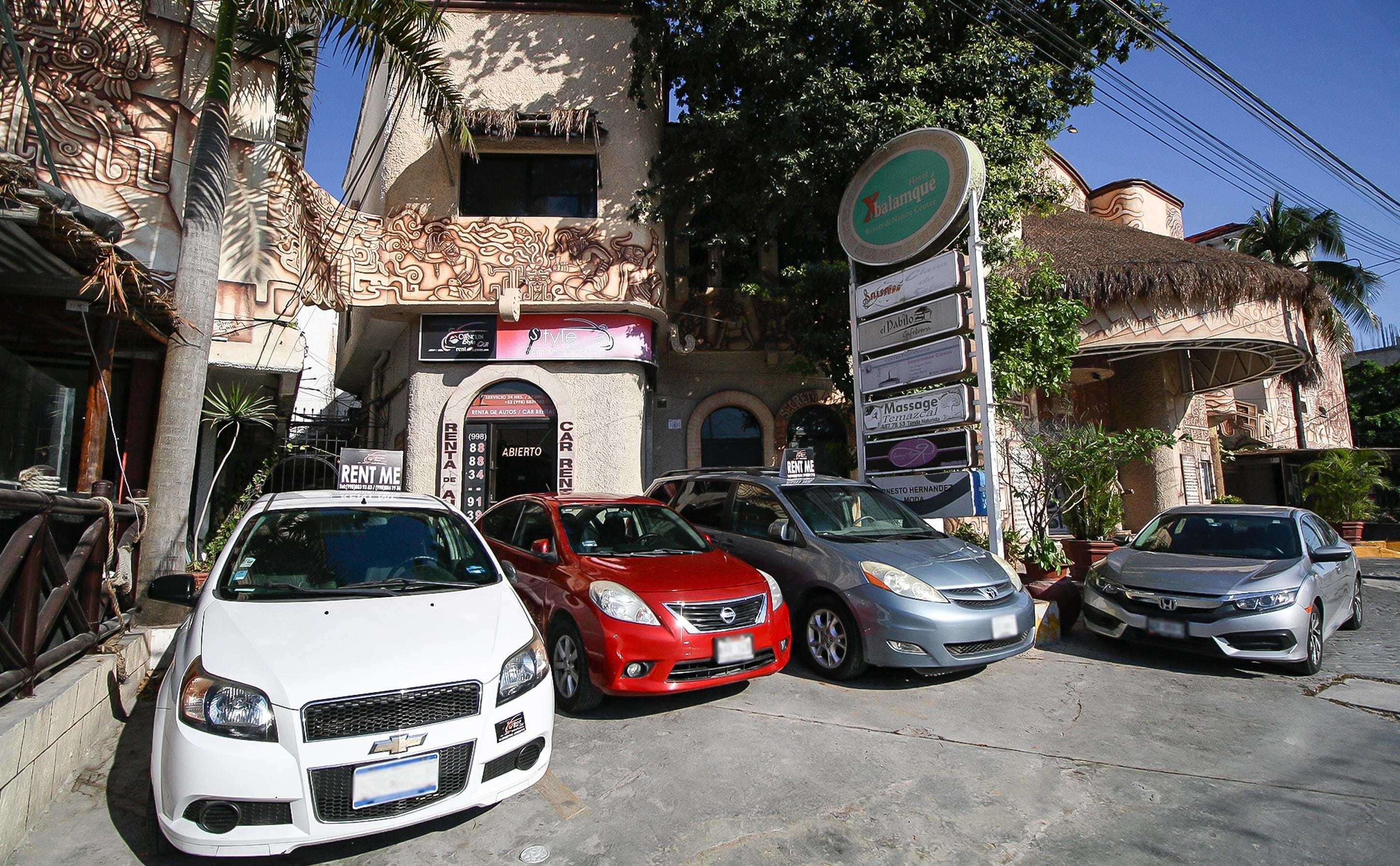Una fila de coches aparcados frente a un edificio con un letrero que dice 'Hotel Xbalanque'.