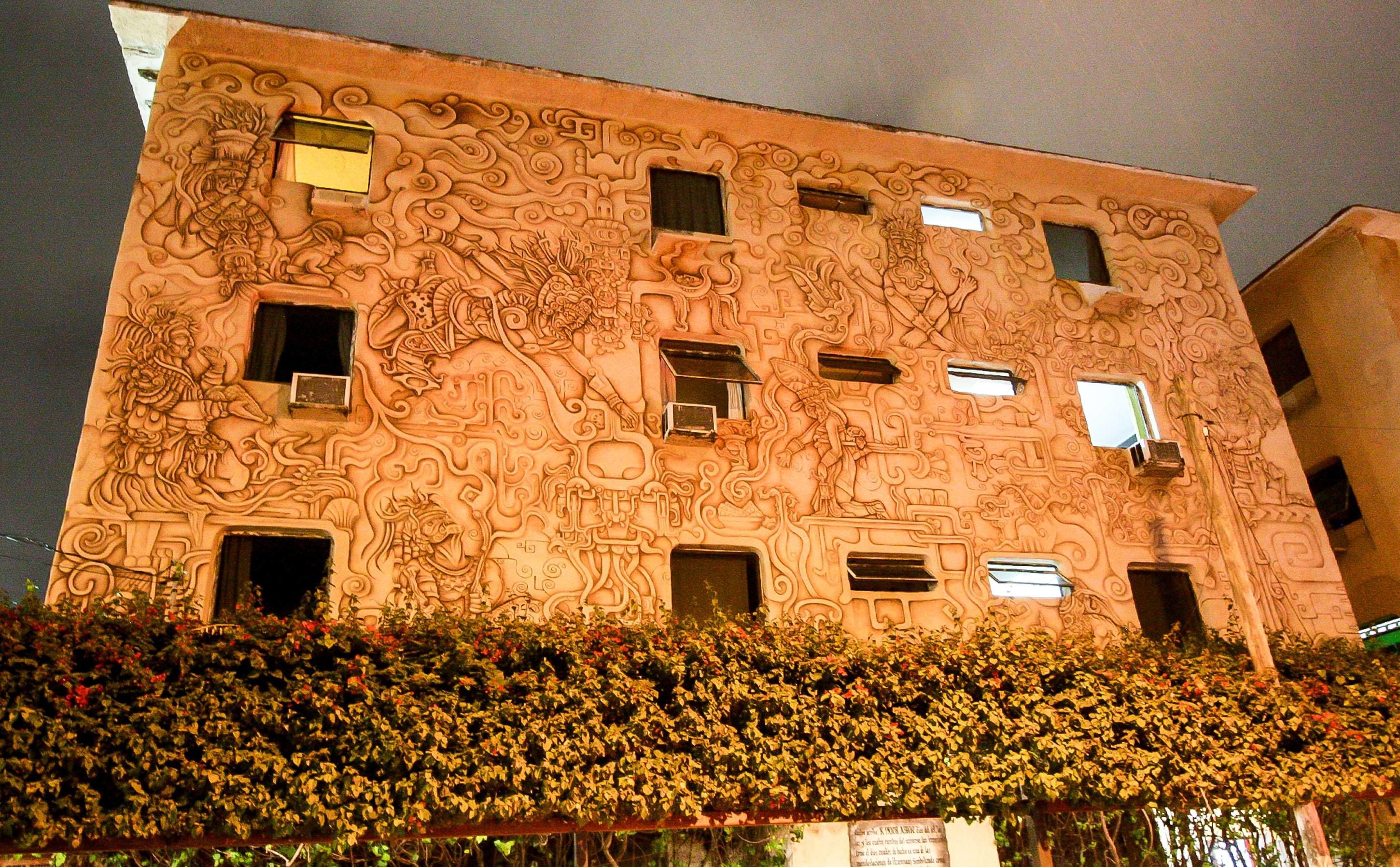 A building with intricate carvings on its facade, multiple windows, and a balcony with plants.