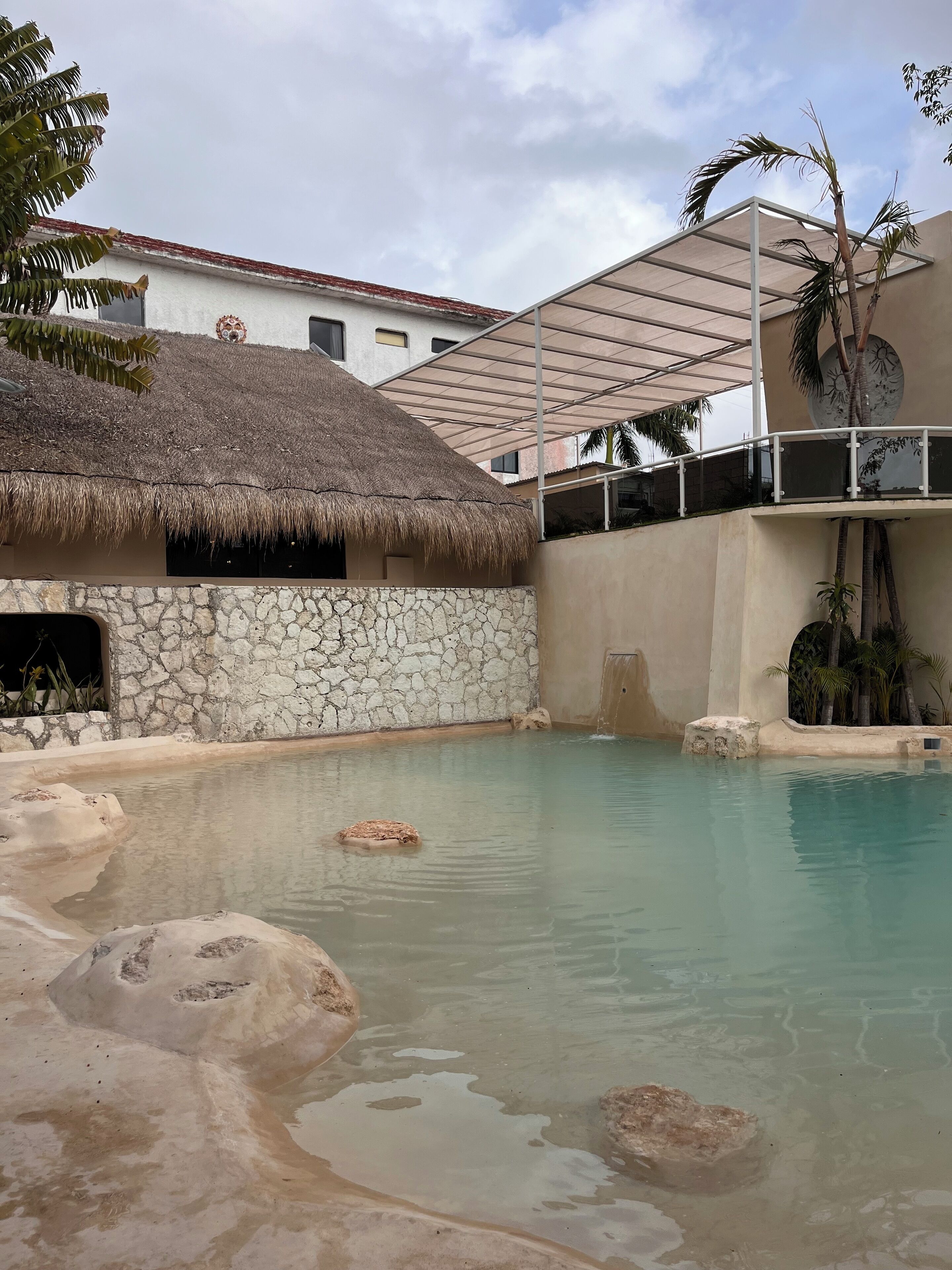 Un espace piscine doté d’une structure avec toit de chaume, de murs en pierre et d’une piscine à eau claire.