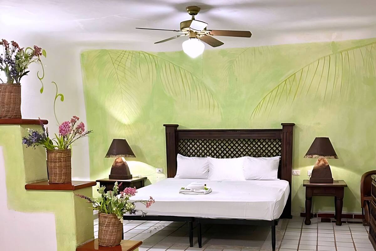 Camera da letto con un letto, due comodini con lampade, una ventola a soffitto e una mensola a parete con fiori.