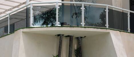 Un espace piscine agrémenté d’une balustrade en verre, de palmiers et d’un mur en pierre.