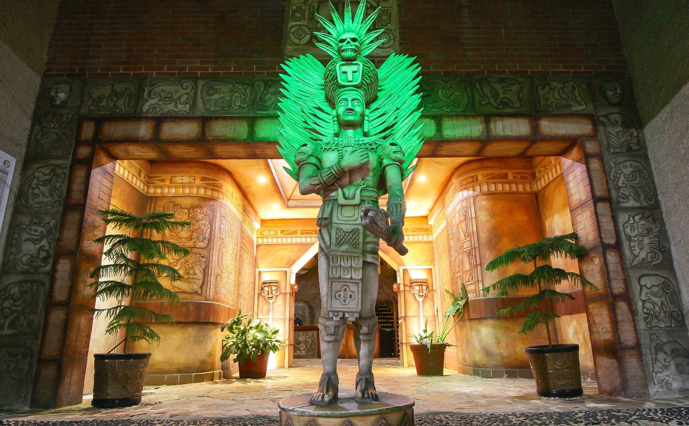 Uma estátua com um cocar verde em um edifício com colunas ornamentadas e paredes estampadas.